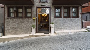 Entrada de un hotel con fachada de piedra, un cartel visible y dos macetas.