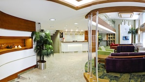 Zona de recepción de hotel con mostrador, asientos y una planta grande en maceta.