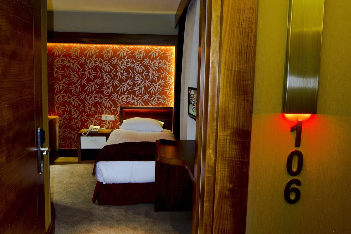 A hotel room with a bed, a bedside table, a phone, a wall with a floral pattern, and a ceiling light.