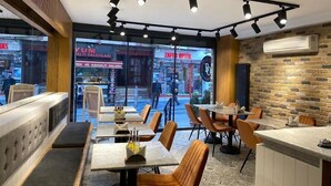 L’intérieur d’un restaurant moderne, avec un mur en briques, de nombreuses tables et chaises, et une vue sur la rue.