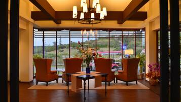 A modern interior with a large window, wooden flooring, and orange chairs around a table with a vase of flowers.