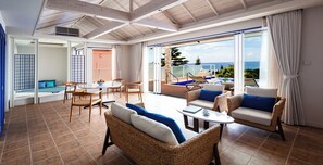 A spacious indoor area with wicker furniture, a dining table, and a view of the ocean through large glass doors. - The Shigira (Miyakojima)