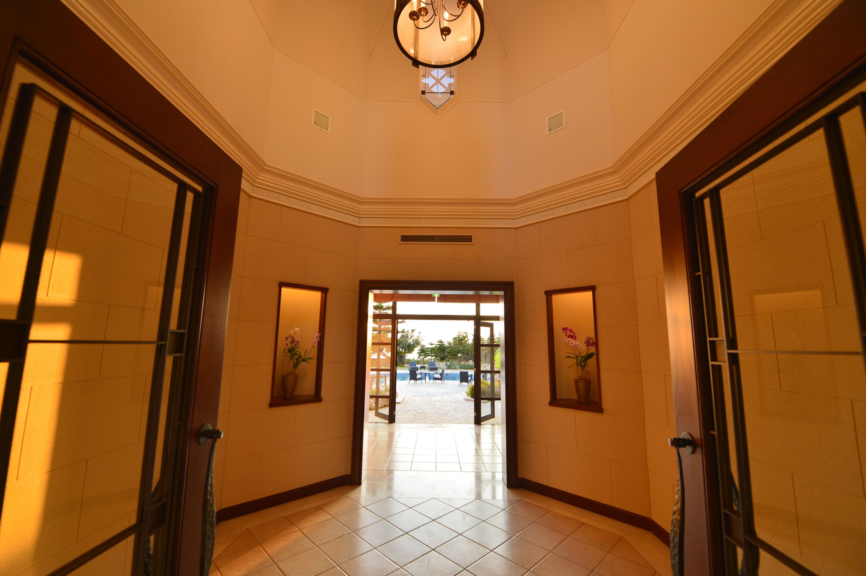 A hotel lobby with a tiled floor, a chandelier, and a view of an outdoor patio with tables and chairs.