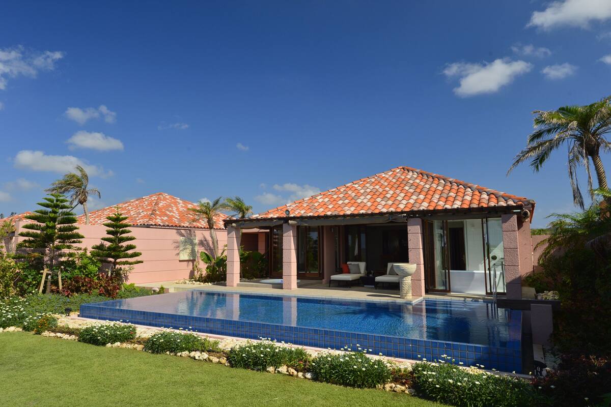 A resort with a swimming pool, palm trees, and a tiled roof.