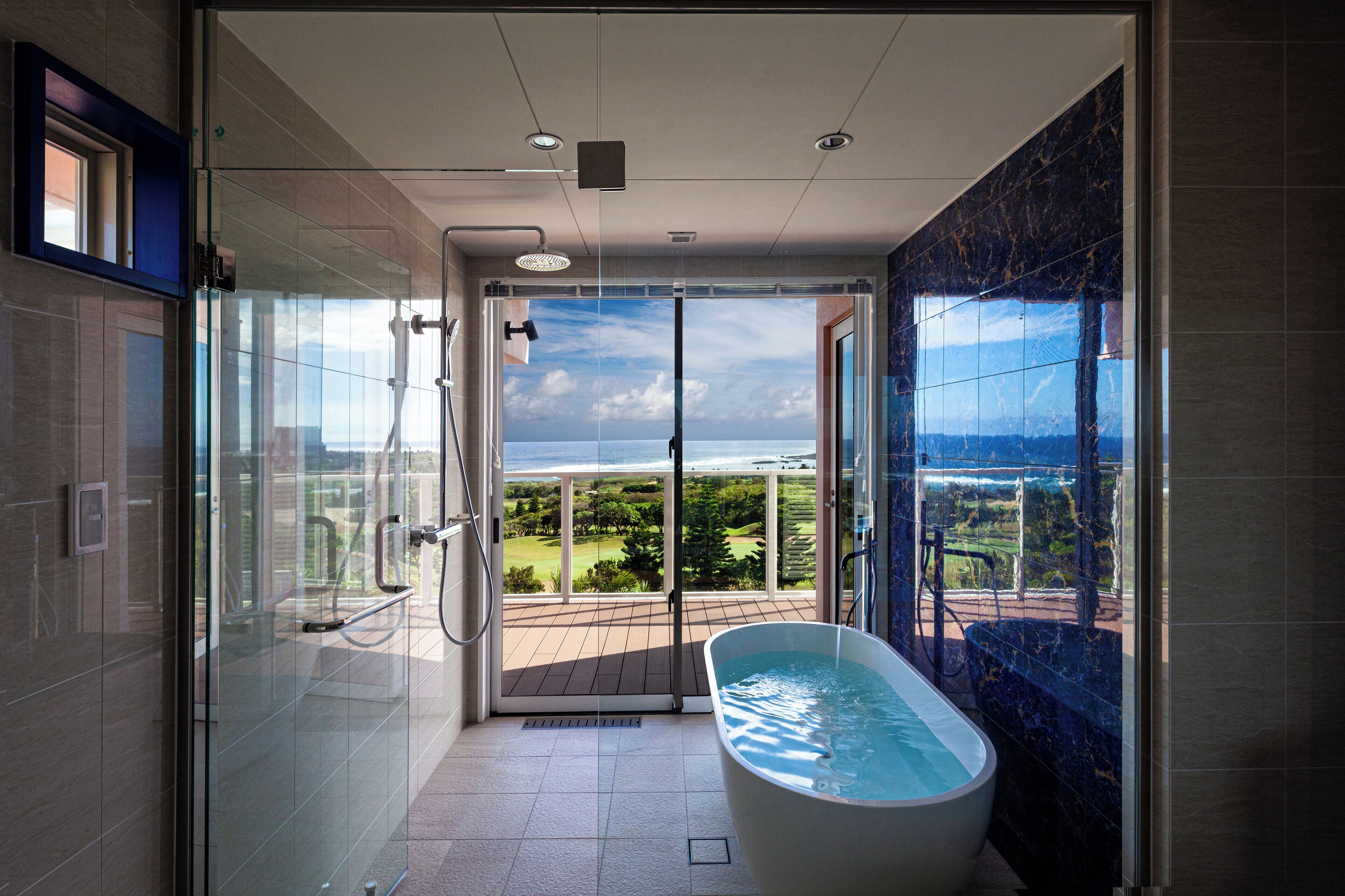 Un baño moderno con ducha envuelta en vidrio, una bañera independiente y vistas a un campo de golf.