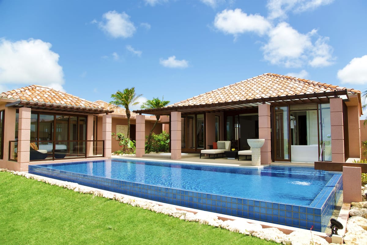 A modern poolside area with a rectangular pool, glass-enclosed cabanas, and a well-maintained lawn.