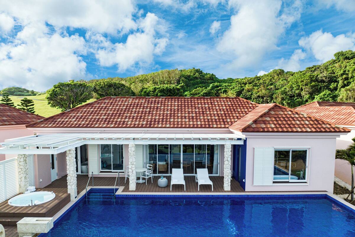 A modern house with a swimming pool, a patio with chairs, and a view of the surrounding greenery.