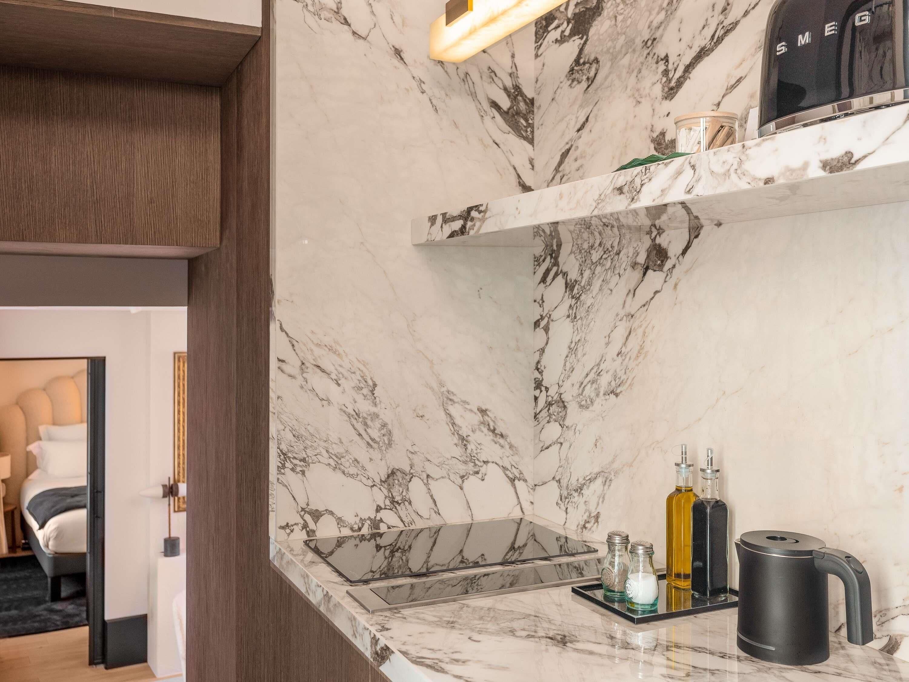A modern kitchen with marble countertops, a built-in stove, and a coffee maker.