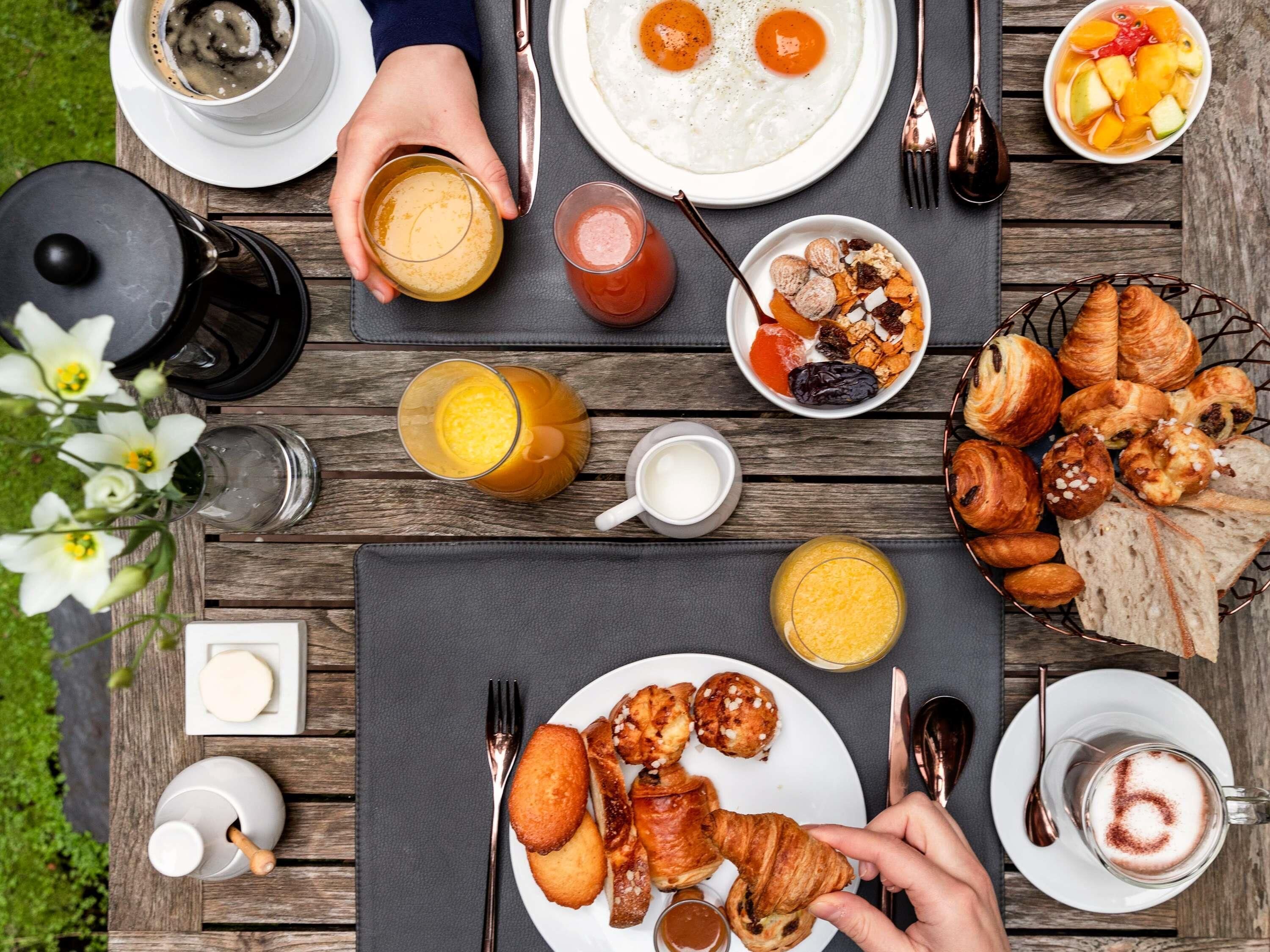 A breakfast table with various foods, drinks, and utensils.