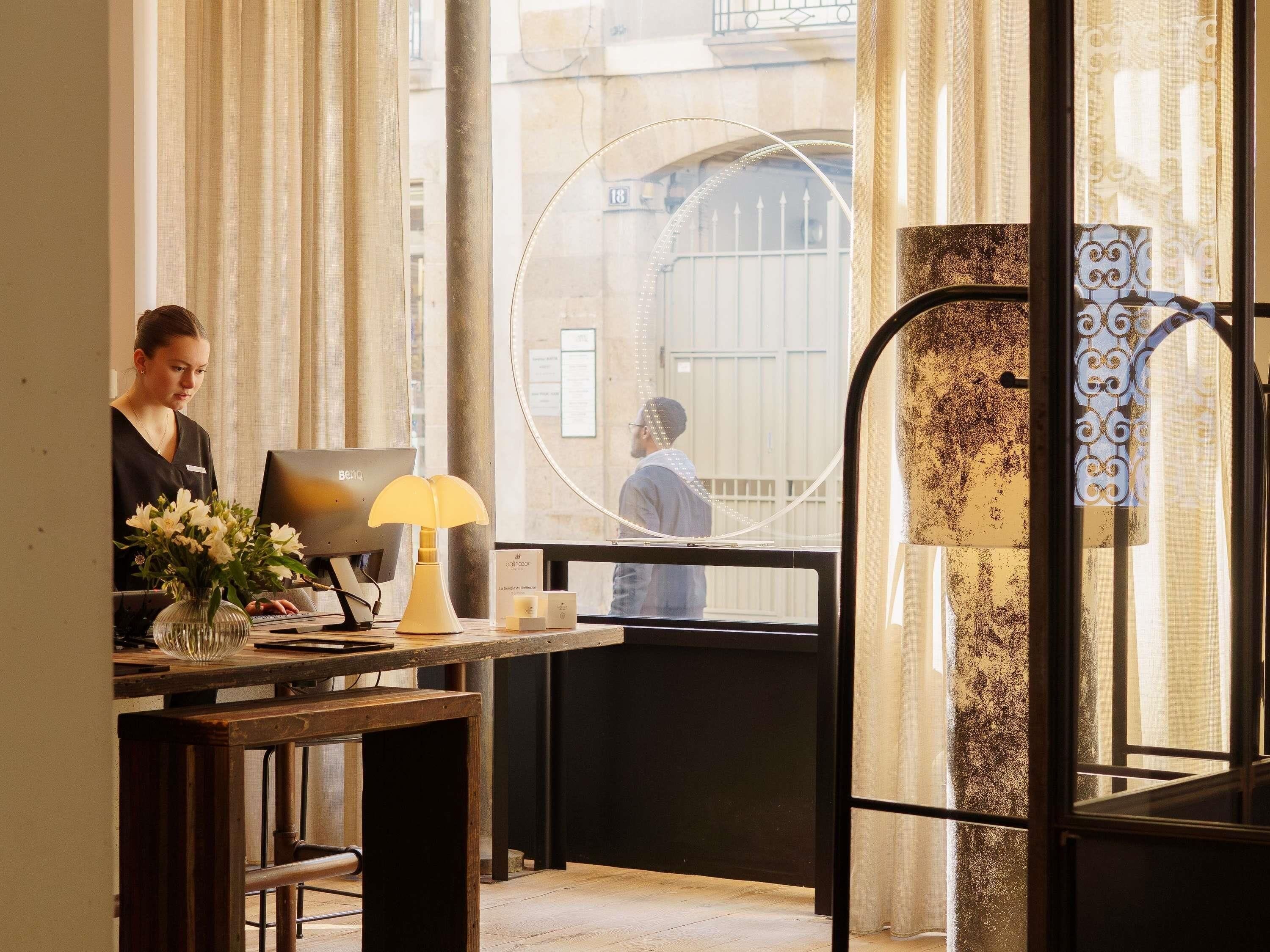 A hotel reception desk with a computer, a vase of flowers, and a lamp.