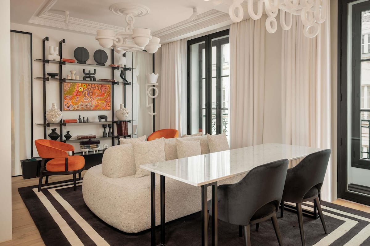 A modern living room with a large L-shaped sofa, a dining table, and a chandelier.
