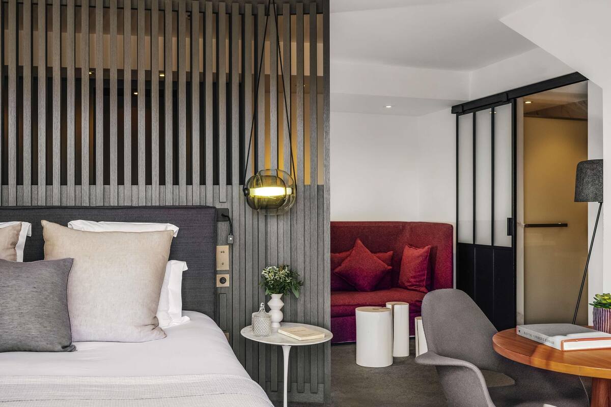 A modern hotel room with a bed, a red sofa, a small round table, and a chair.