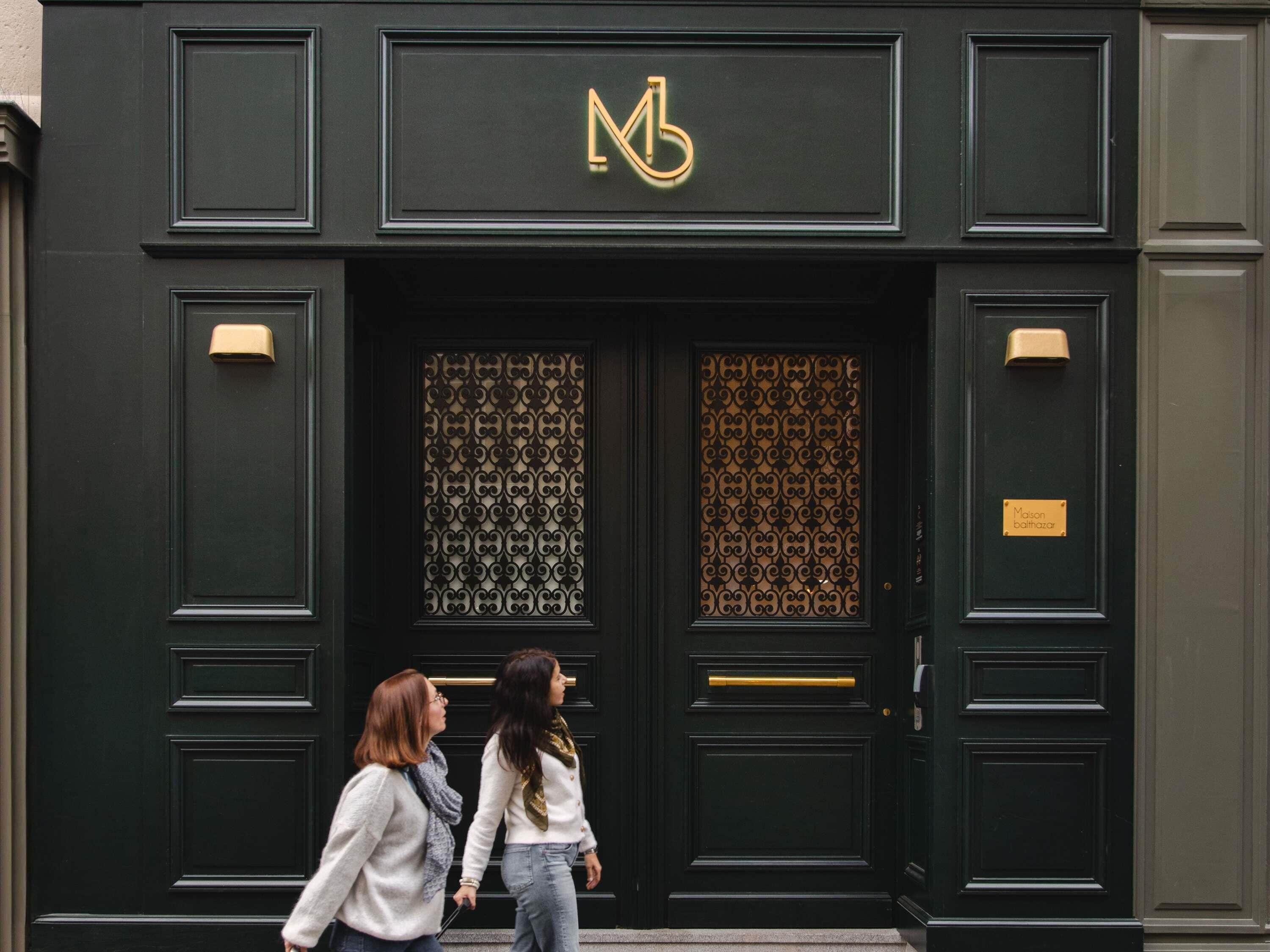 A building facade with a prominent 'MB' logo, a decorative door with intricate patterns, and a nameplate reading 'Mason Bathhouse.'