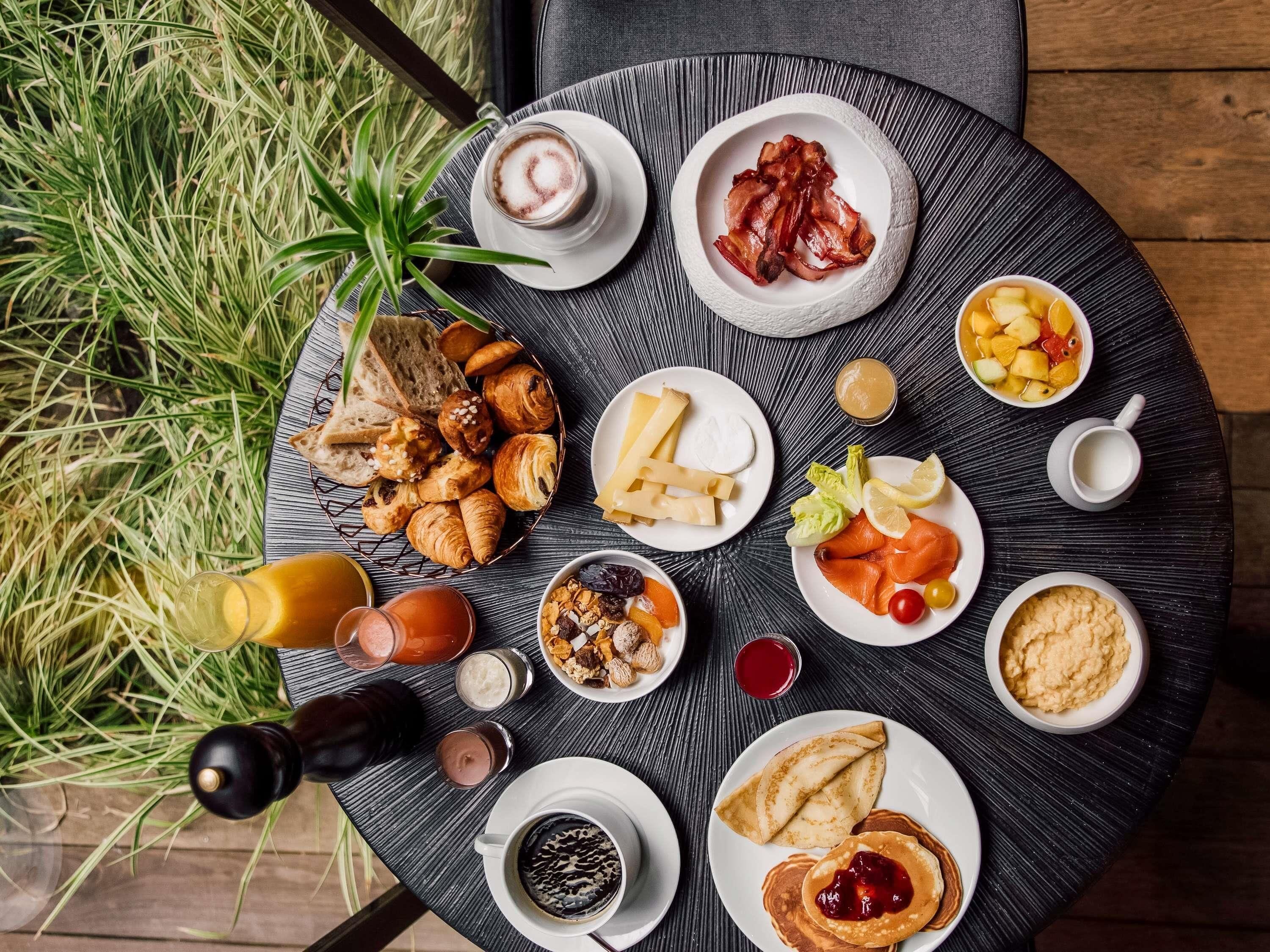 Mesa redonda para refeições com diversos itens de café da manhã, incluindo pães, salmão defumado e panquecas.
