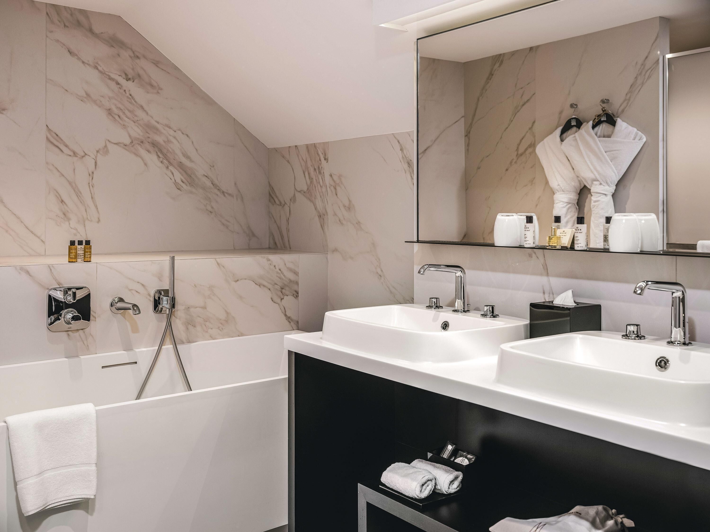 A modern bathroom with two sinks, a large mirror, and a bathtub.