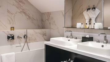 A modern bathroom with two sinks, a large mirror, and a bathtub.