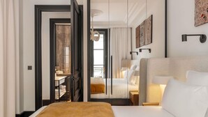 A hotel room with a large bed, a smaller bed, a desk with a chair, and a bathroom with a mirror and towel rack. - Balthazar Hotel & Spa Rennes - MGallery Collection (Rennes)