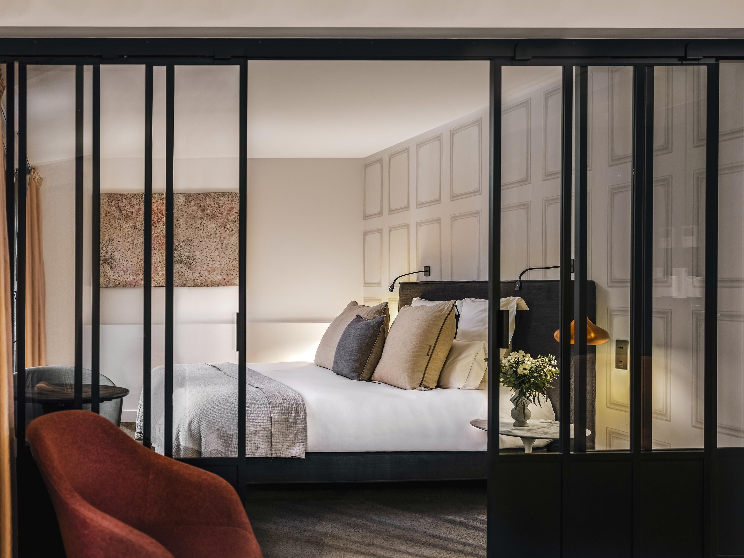 A modern hotel room with a bed, a desk, a chair, and a decorative wall piece.