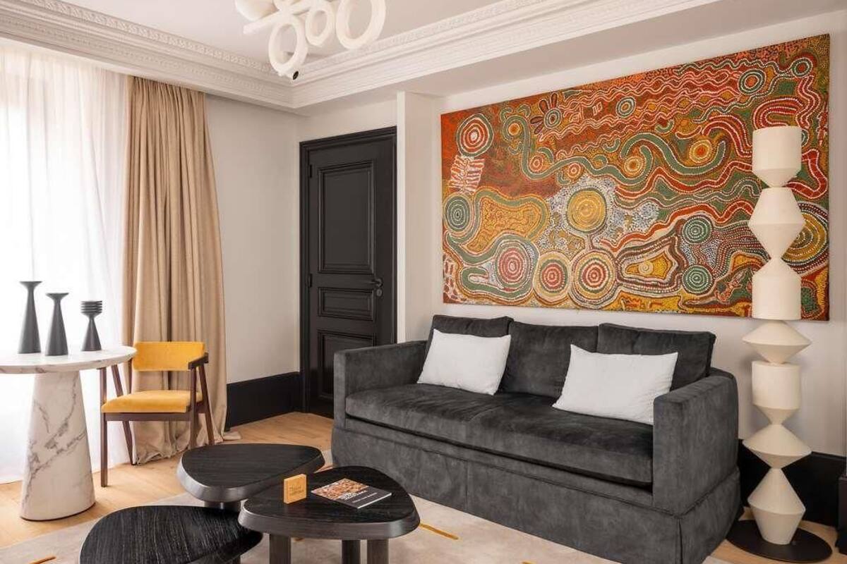 A modern living room with a grey sofa, a round coffee table, a yellow chair, a white floor lamp, and a large abstract painting on the wall.