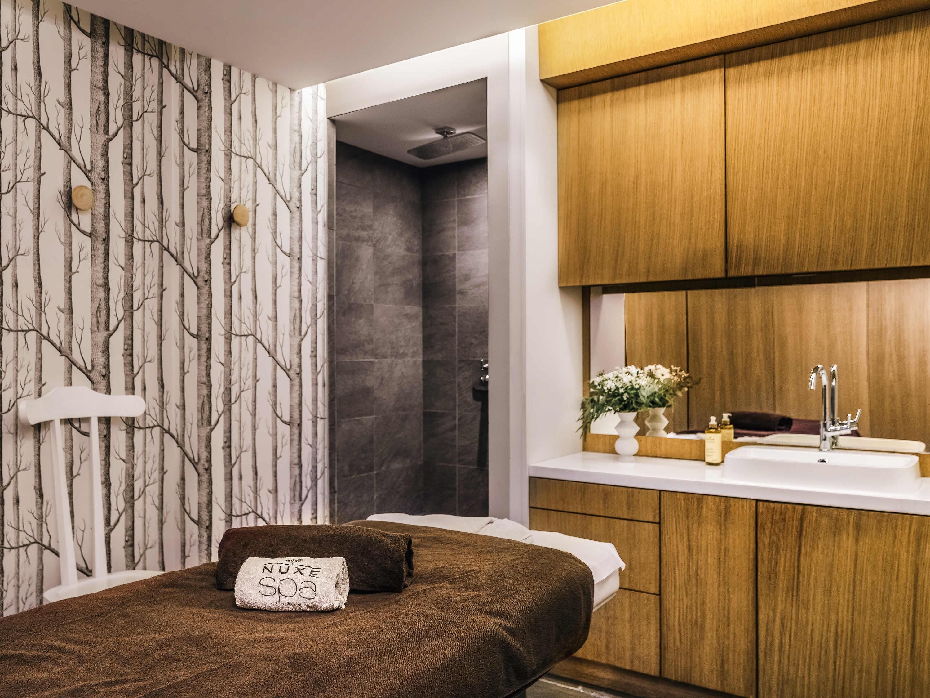 Un baño moderno con ducha, un lavabo con espejo y una toalla con el texto 'NUXE spa'.