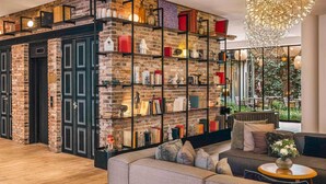 A modern living room with a brick wall bookshelf, a grey sofa, and a round wooden side table. - Balthazar Hotel & Spa Rennes - MGallery Collection (Rennes)