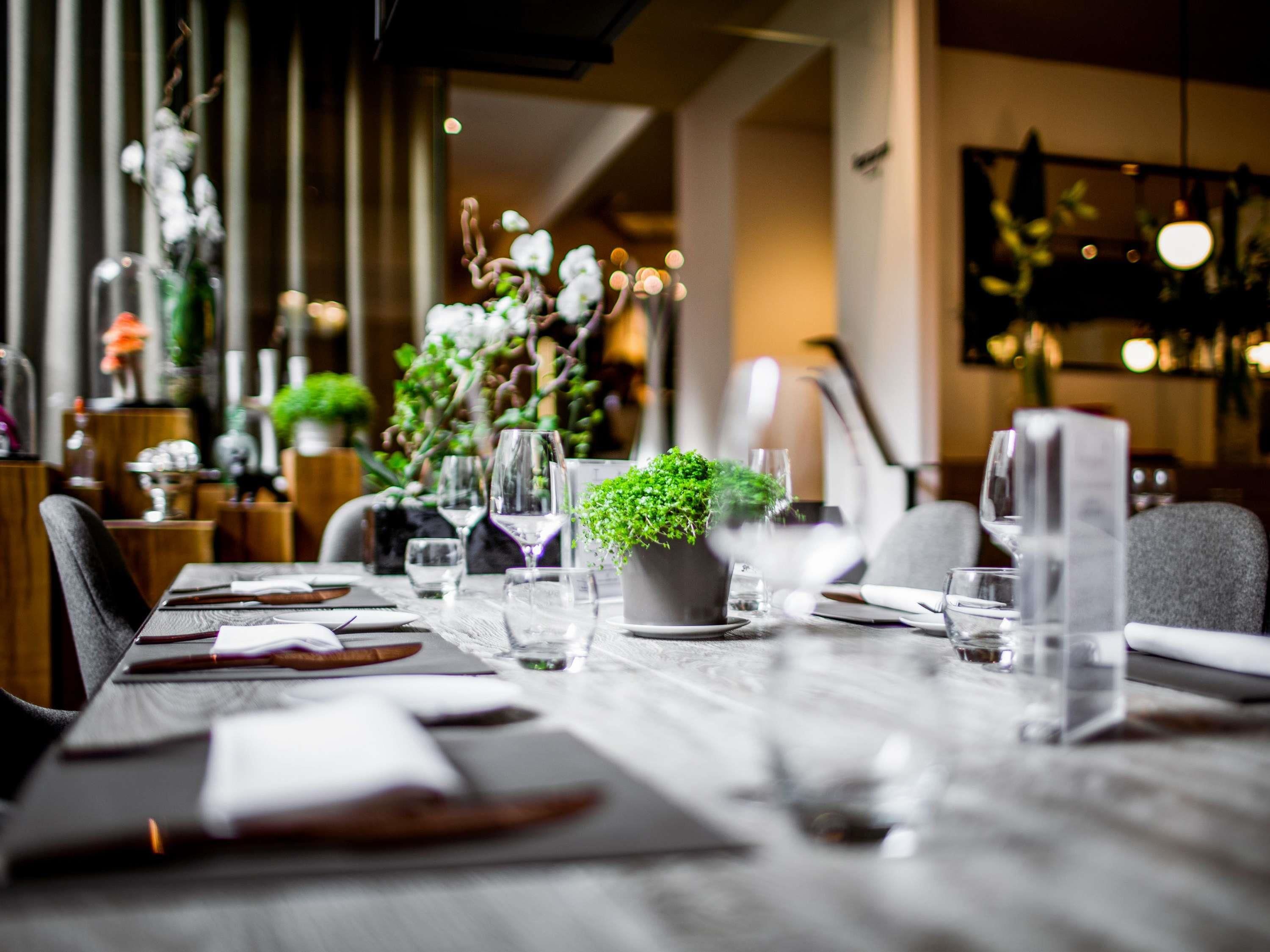Mesa de restaurante posta com copos de vinho, pratos e um vaso de planta.