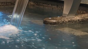 A modern water feature with a curved metal structure in a pool, set against a textured stone wall. - Balthazar Hotel & Spa Rennes - MGallery Collection (Rennes)
