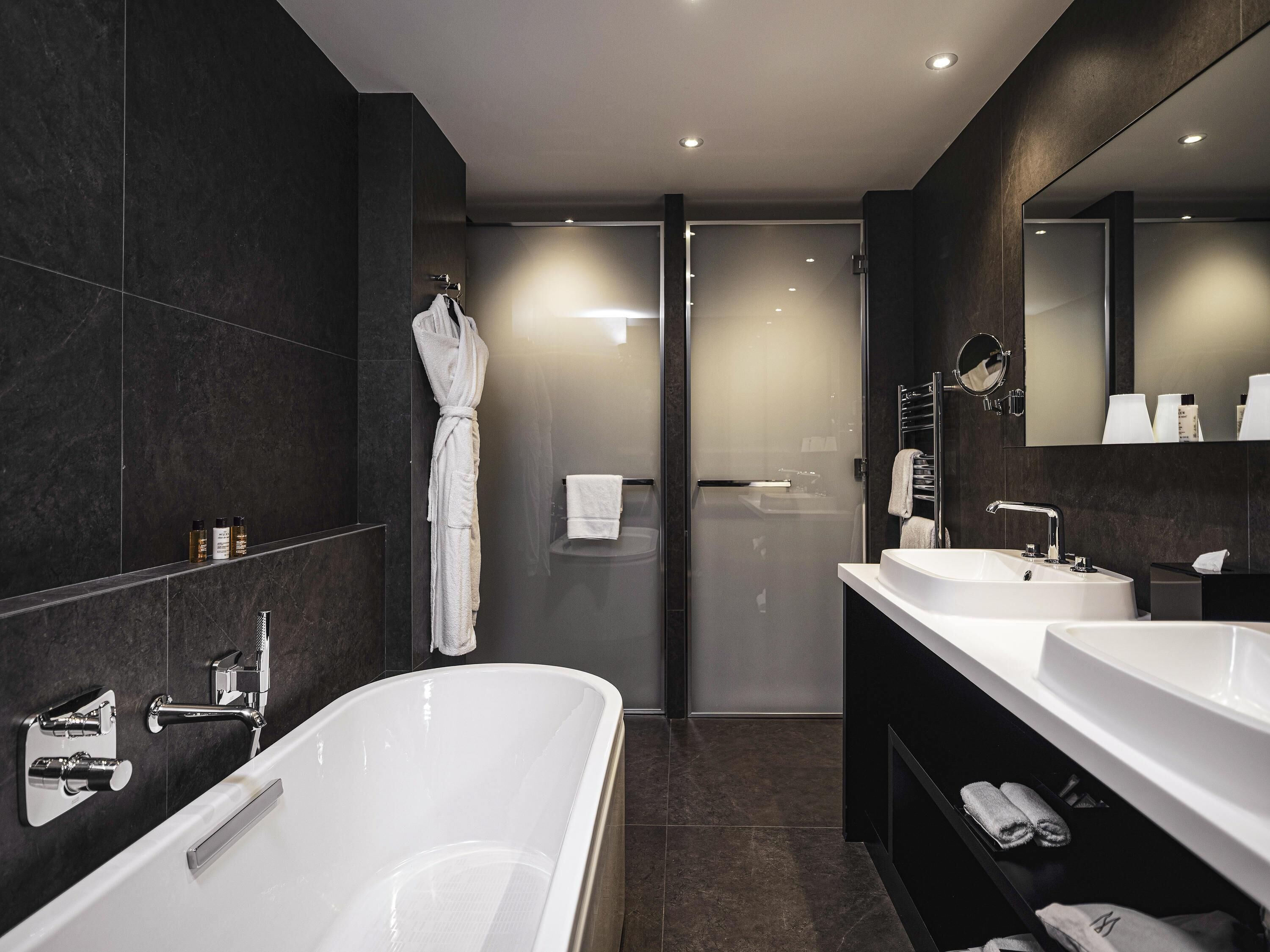 A modern bathroom with a large bathtub, two sinks, and a glass shower enclosure.