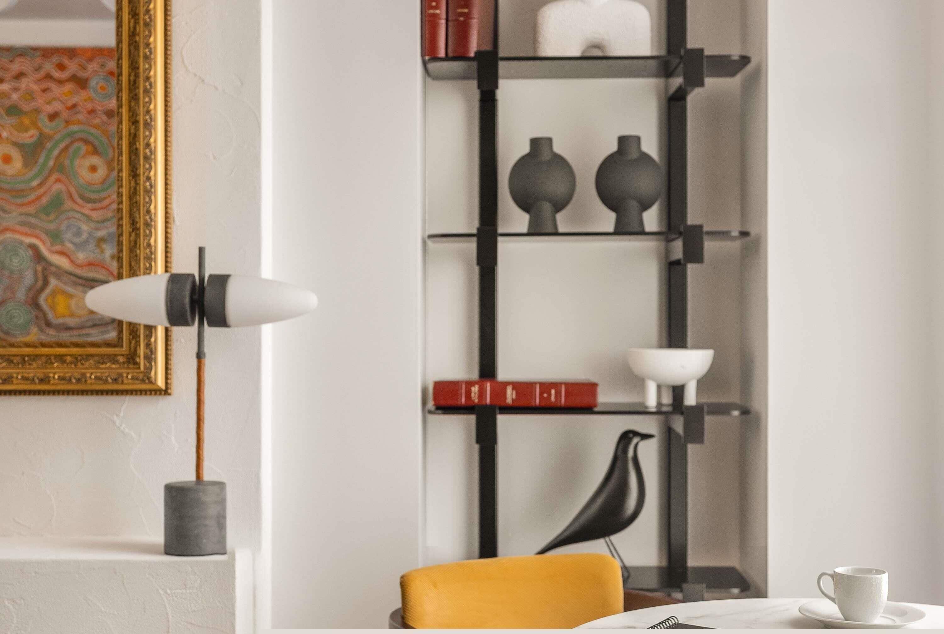 A modern interior with a black metal shelving unit, a white table with a cup, and a yellow chair.