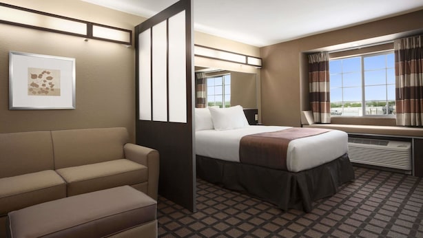 A hotel room with a bed, a sofa, a window with curtains, and a framed picture on the wall. - Microtel Inn & Suites by Wyndham Kenedy/Karnes City (Kenedy)