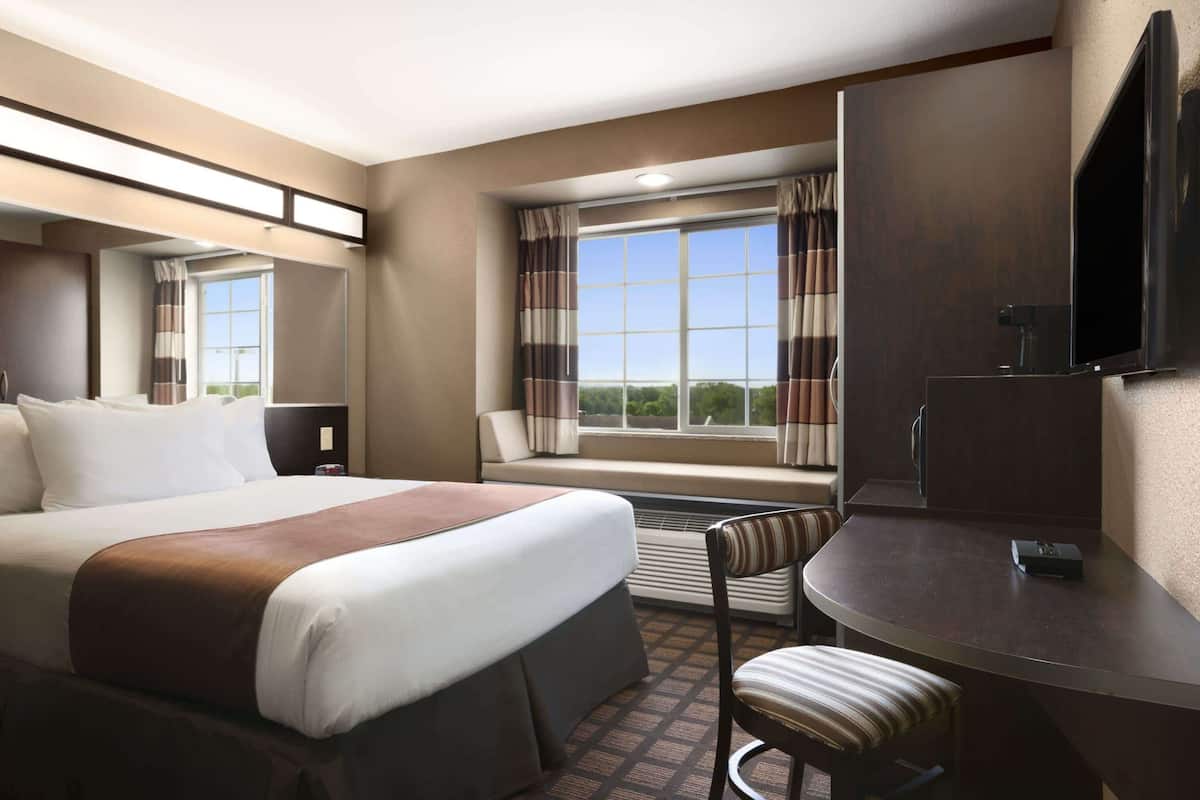 A hotel room with a large bed, a desk with a chair, a TV, and a window with curtains.
