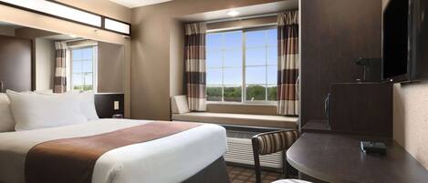 A hotel room with a large bed, a desk with a chair, a TV, and a window with curtains.