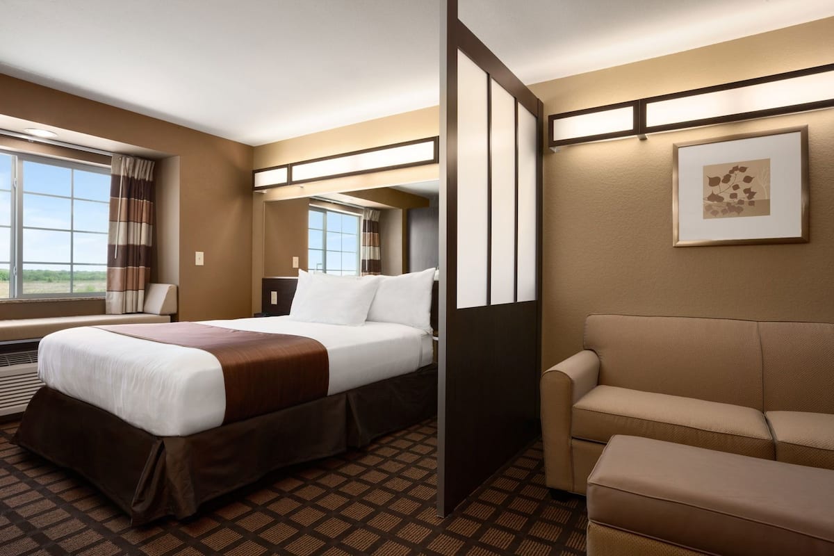 A hotel room with a bed, a sofa, a large window, a mirror, and a framed picture on the wall.