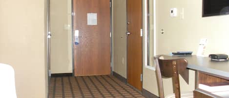 A hotel room with a bed, a desk, a chair, a wooden door, and a patterned floor.