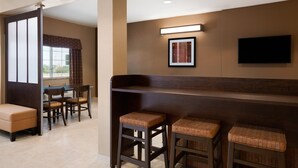 A hotel lobby with a seating area, a television mounted on the wall, and a window with curtains. - Microtel Inn & Suites by Wyndham Kenedy/Karnes City (Kenedy)