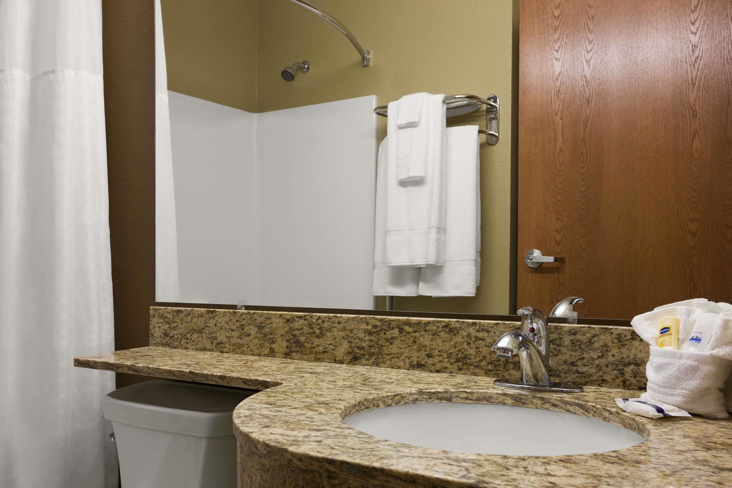 A bathroom with a granite countertop sink, a mirror, a towel rack, and a shower curtain.