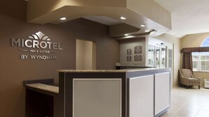 A reception area with a counter, a seating area with a chair, and a wall with the hotel name and amenities. - Microtel Inn & Suites by Wyndham Kenedy/Karnes City (Kenedy)