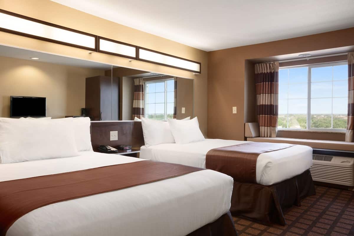 A hotel room with two beds, a TV, a desk, and a large window with curtains.