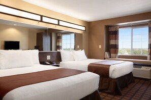 A hotel room with two beds, a TV, a desk, and a window with curtains.