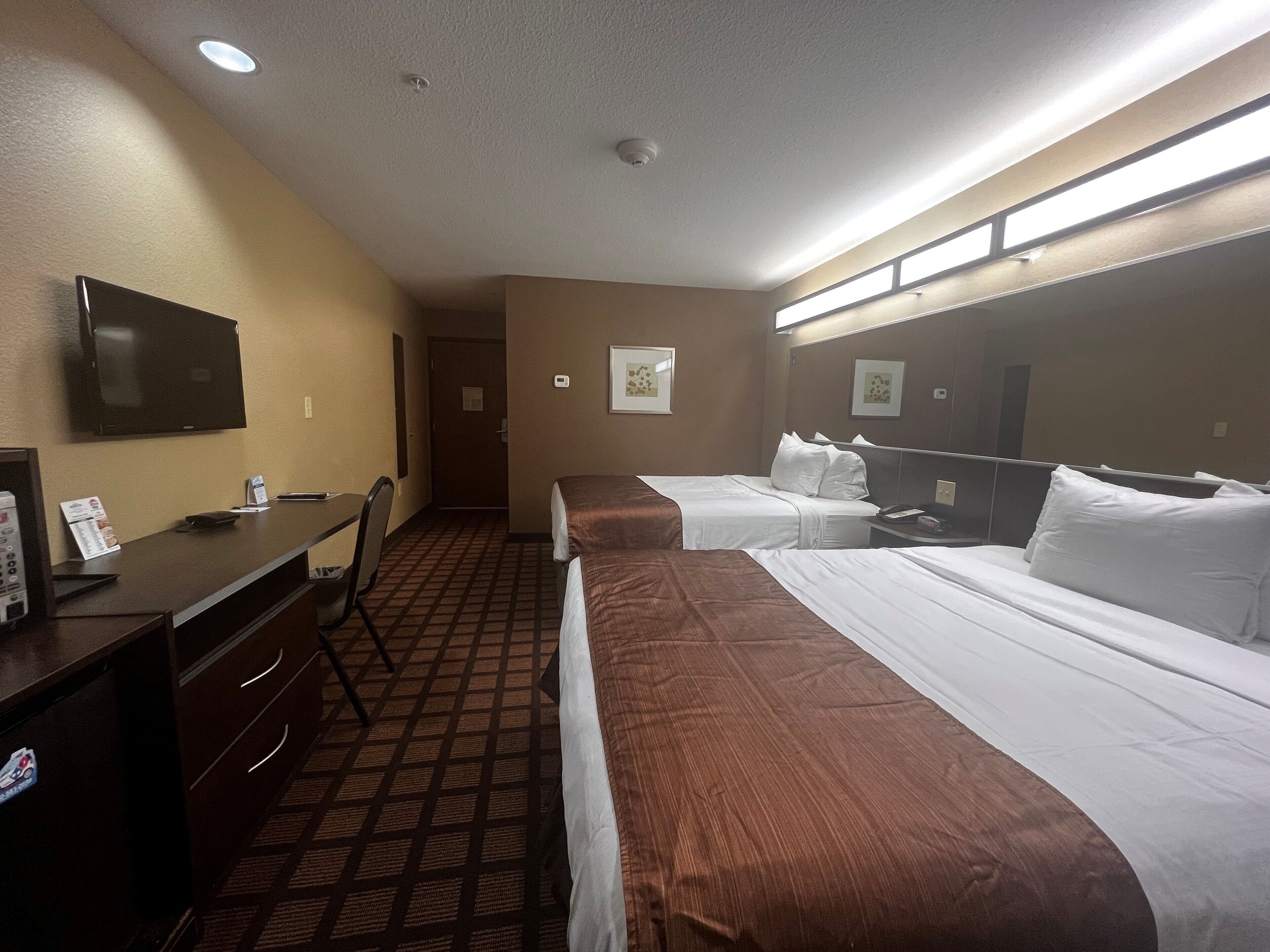 A hotel room with two beds, a desk, a chair, a television, and a bathroom door.