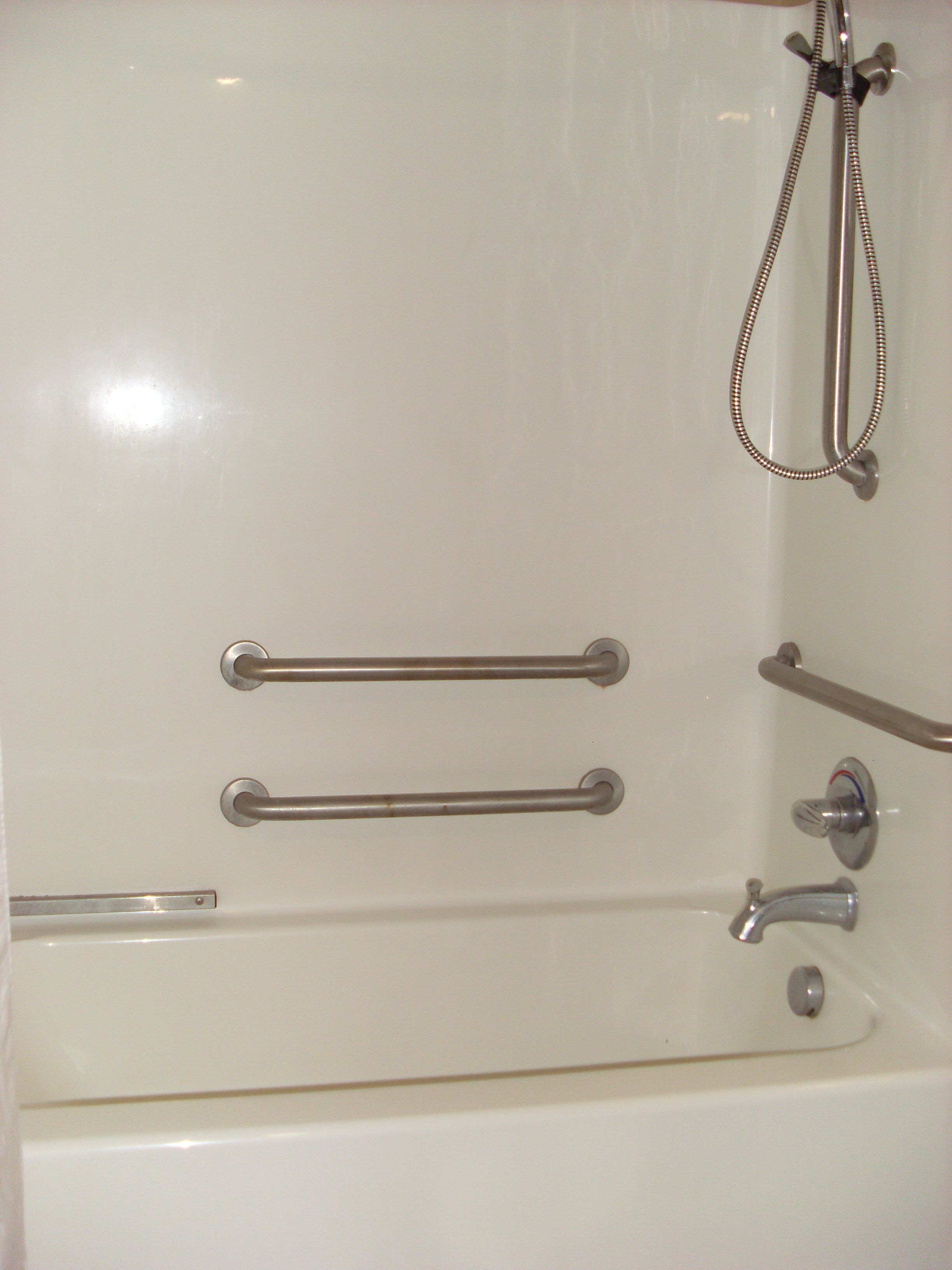A white bathtub with grab bars, a showerhead, and a faucet.