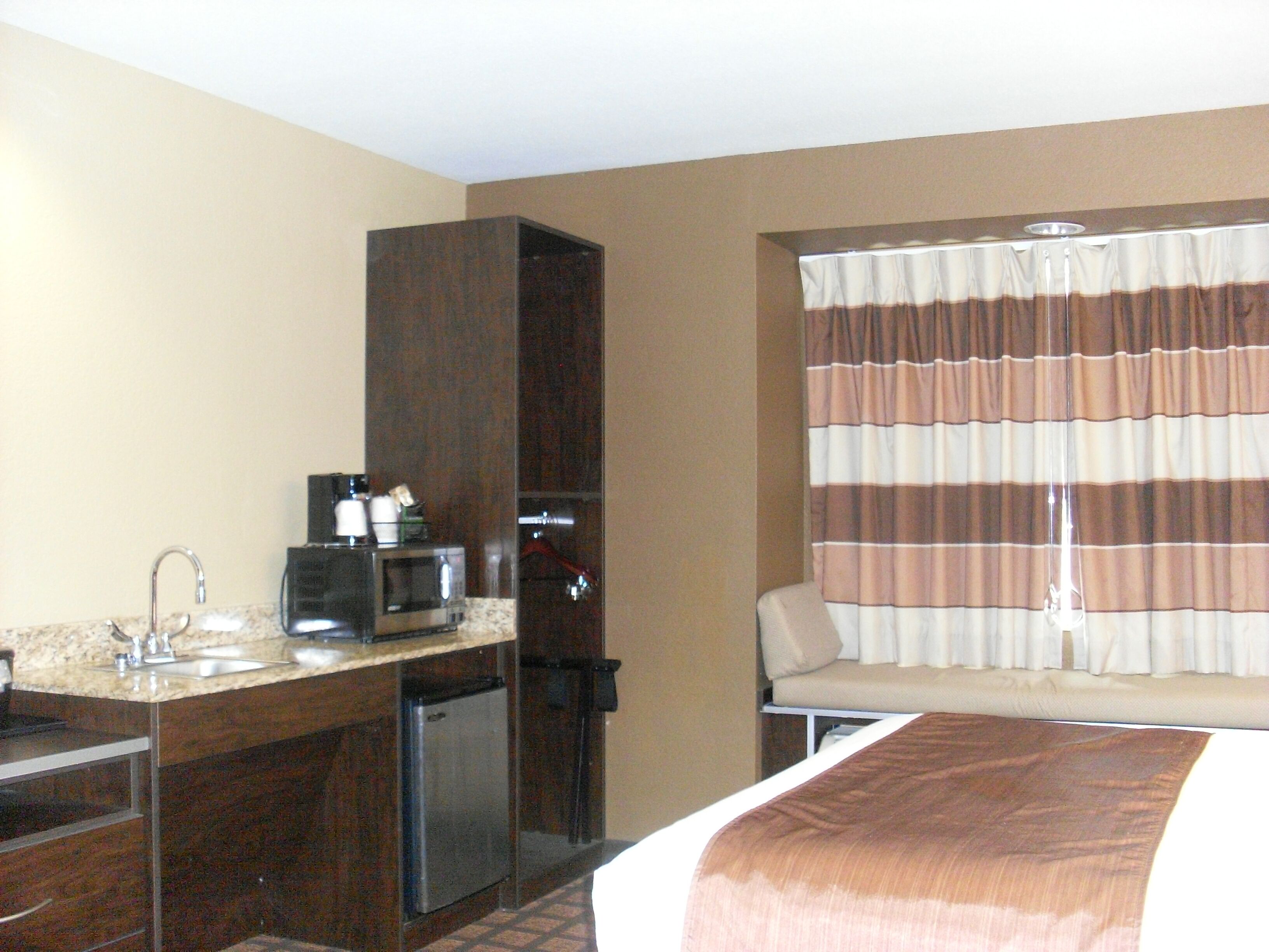 A hotel room with a kitchenette, a bed, a window with striped curtains, and a sofa.