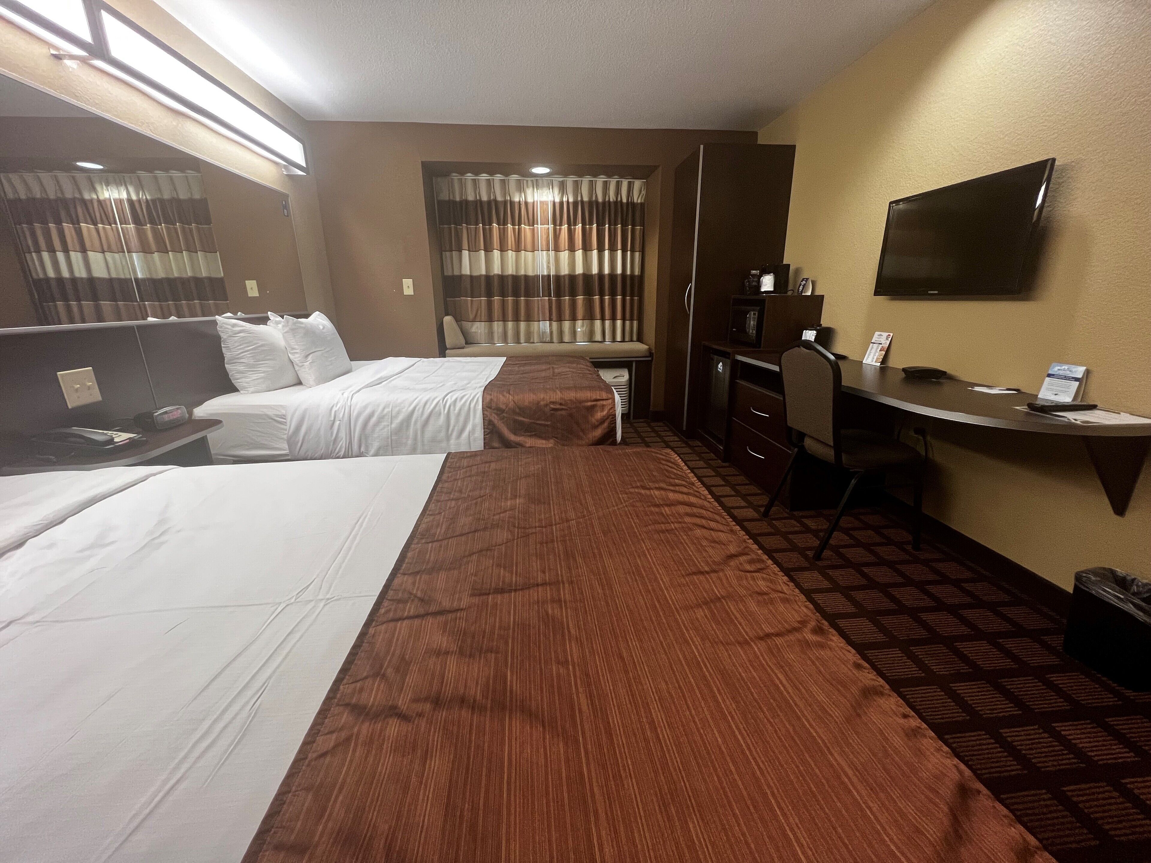 A hotel room with two beds, a desk, a TV, and a window with curtains.
