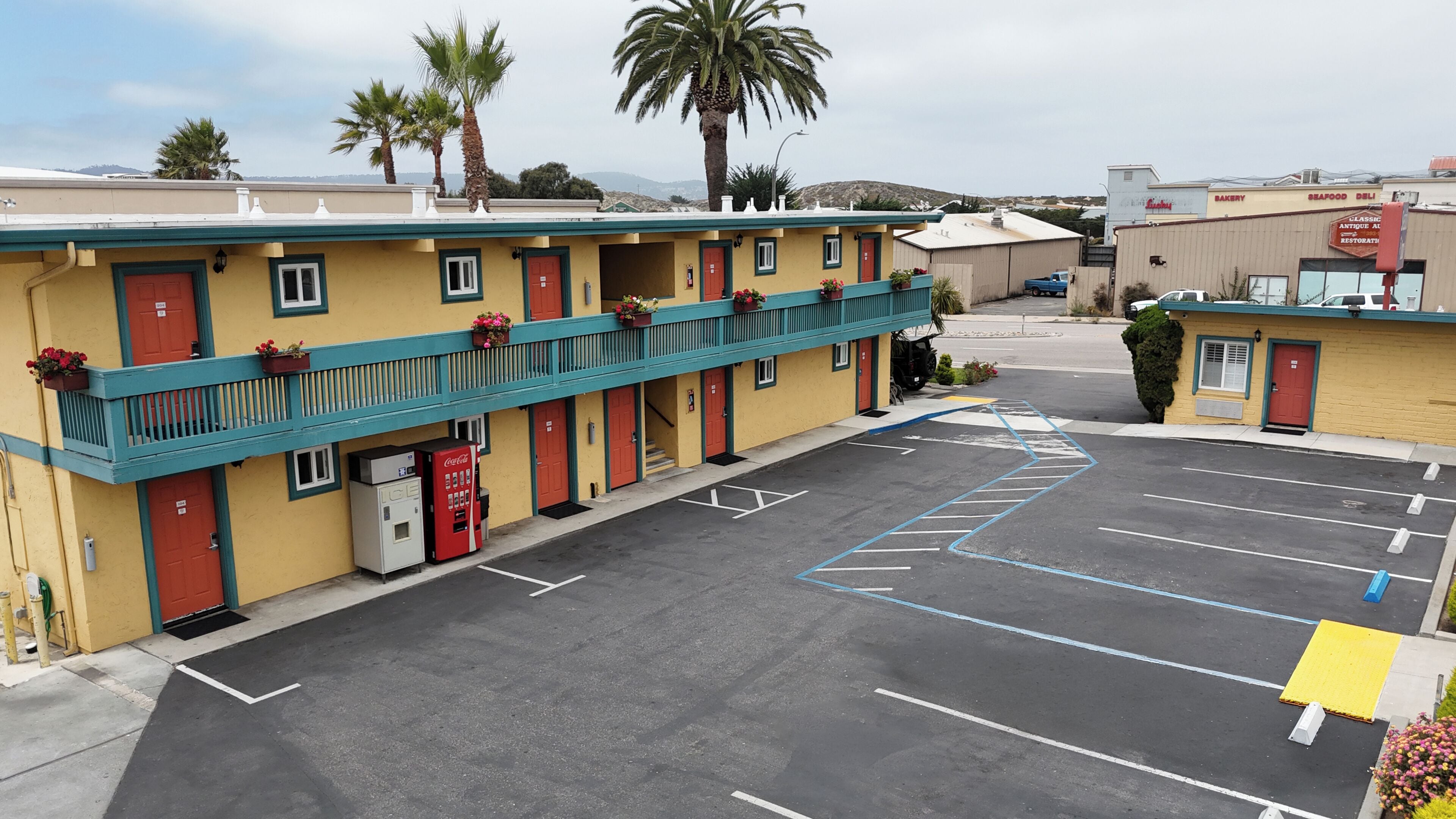 Un motel con un estacionamiento, una máquina expendedora de Coca-Cola y un letrero que anuncia una panadería y un deli de mariscos.