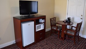 A compact room with a flat-screen TV on a wooden cabinet, a mini-fridge, a microwave, and a small table with chairs. - Seaside Inn (Seaside)