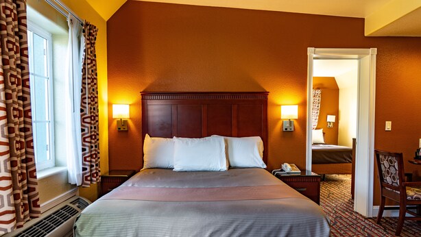 A hotel room with a large bed, two bedside lamps, a chair, and a desk. - Seaside Inn (Seaside)