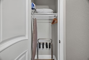 Un vestidor con una percha, un perchero y un estante con una almohada blanca y una plancha.