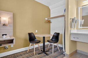 Habitación de hotel con cama, mesita de noche con lámpara, espejo en la pared, pequeña mesa redonda con dos sillas y piso alfombrado.