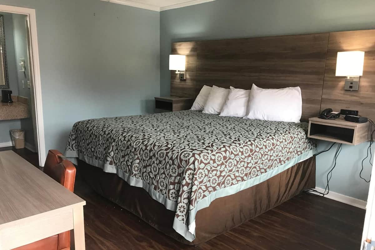 Quarto com uma cama grande, duas mesas de cabeceira com luminárias, uma cabeceira de madeira e um pequeno criado-mudo de madeira com um telefone e um rádio.