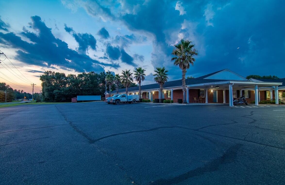 Ein Motel mit überdachtem Parkplatz, Palmen und blauem Himmel.